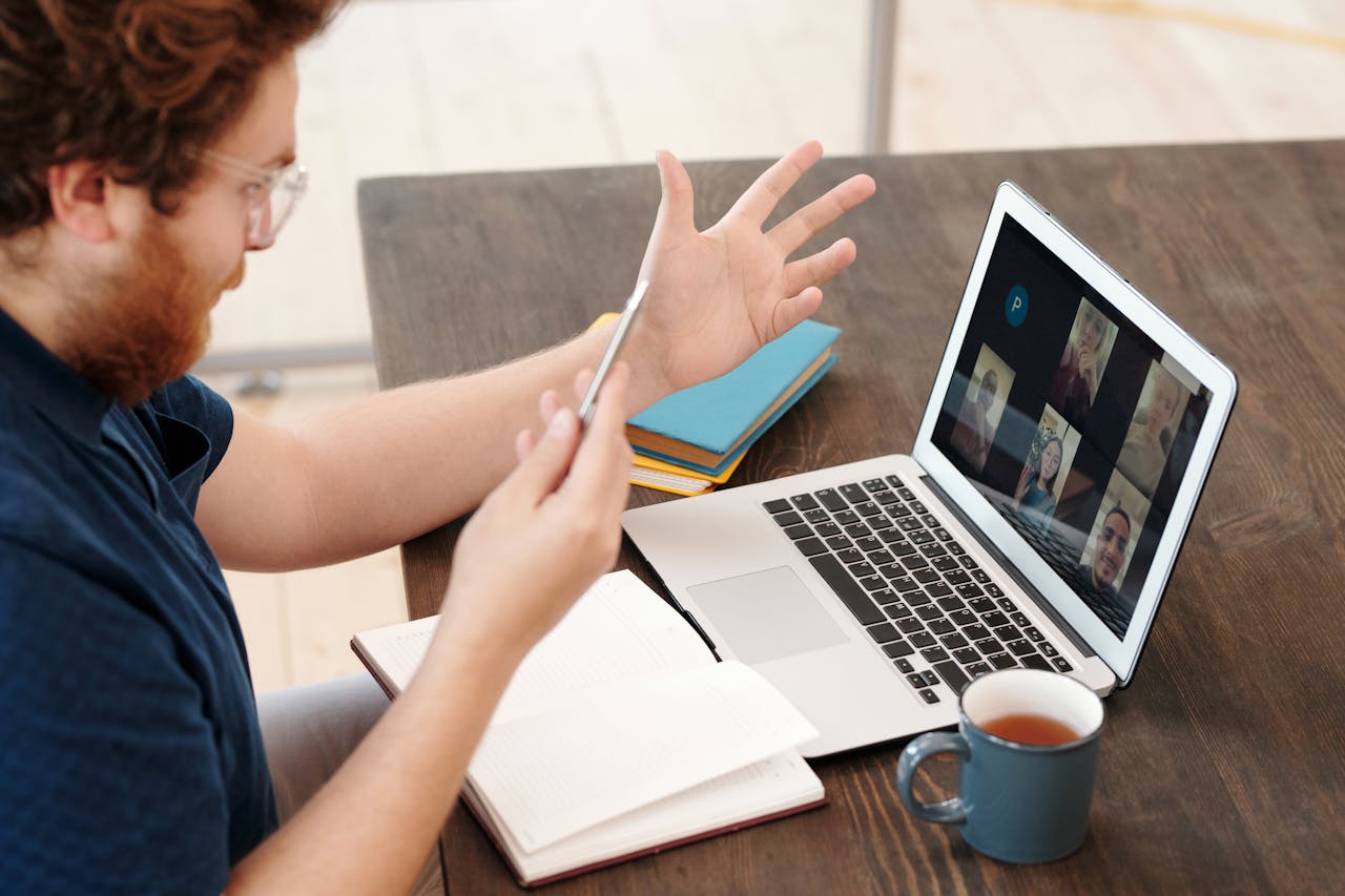 Man engaged in a virtual meeting at home with laptop and tea, chatting and studying online.